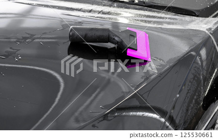 Car wrapping specialist putting vinyl foil or film on car. Protective film on the car. Applying a protective film to the car with tools. Car detailing. Transparent film. Car paint protection. Trimming 125530661