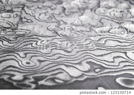 Background with pattern of damask steel. Close up. Macro shot of a damascus knife blade texture. Damascus steel pattern. Metal and steel background. Damascus steel with original pattern. Background with pattern of damask steel. Close up. Macro shot of a damascus knife blade texture. Damascus steel pattern. Metal and steel background. Damascus steel with original pattern. 125530714
