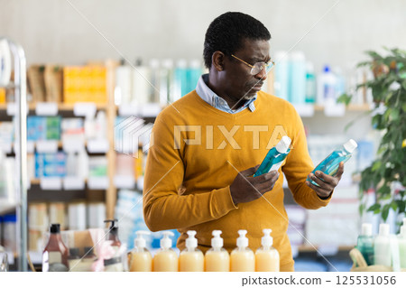 In sales area of pharmacy, African man examines packaging of mouthwash In sales area of pharmacy, African man examines packaging of mouthwash 125531056