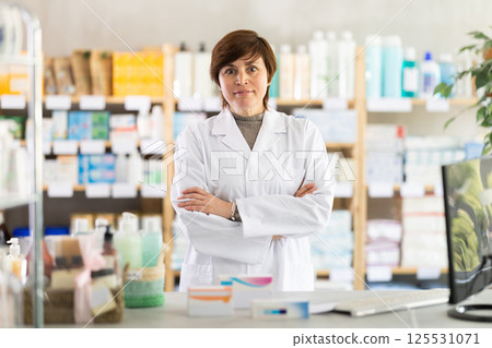 Confident female pharmacist standing behind counter with arms crossed 125531071