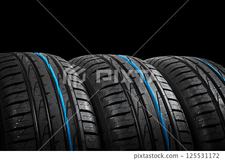 Studio shot of a set of summer car tires on black background. Tire stack background. Car tyre protector close up. Black rubber tire. Brand new car tires. Close up black tyre profile. Car tires in a 125531172