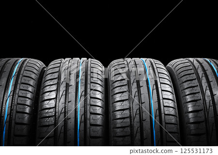 Studio shot of a set of summer car tires on black background. Tire stack background. Car tyre protector close up. Black rubber tire. Brand new car tires. Close up black tyre profile. Car tires in a 125531173