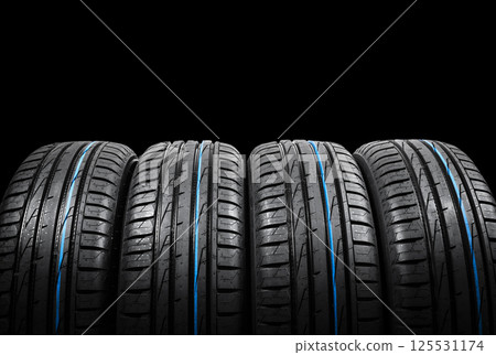 Studio shot of a set of summer car tires on black background. Tire stack background. Car tyre protector close up. Black rubber tire. Brand new car tires. Close up black tyre profile. Car tires in a 125531174