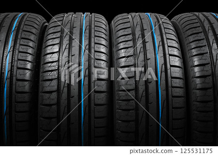 Studio shot of a set of summer car tires on black background. Tire stack background. Car tyre protector close up. Black rubber tire. Brand new car tires. Close up black tyre profile. Car tires in a 125531175