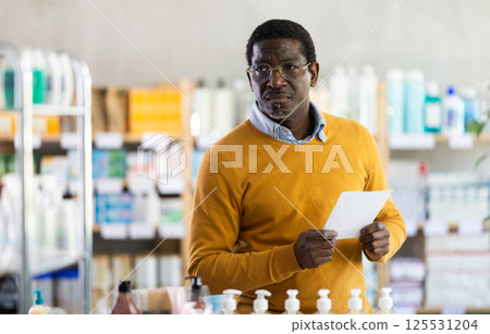 In sales area of drugstore, African man with prescription looks at display cases In sales area of drugstore, African man with prescription looks at display cases 125531204