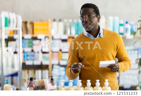 Man in glasses attentively carefully selects pills in modern pharmacy 125531233
