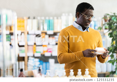 Man in glasses attentively carefully selects pills in modern pharmacy 125531235