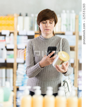 Female shopper in winter clothes scans QR code on label of food for small children using smartphone Female shopper in winter clothes scans QR code on label of food for small children using smartphone 125531283