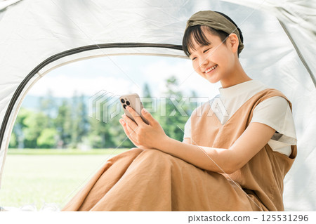 A girl looking at her smartphone in a tent at a campsite 125531296