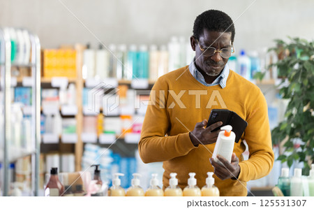 African man in pharmacy scans QR code on cream 125531307