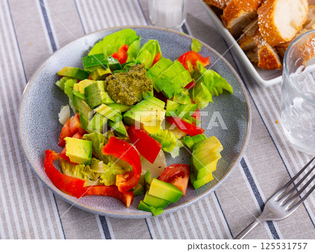 Plate contains portion of salad from fresh vegetables and pesto sauce. 125531757