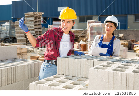 Female builders with hollow concrete blocks in outdoor warehouse Female builders with hollow concrete blocks in outdoor warehouse 125531899