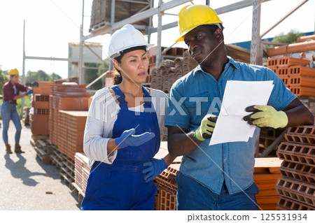 Female builders discuss documentation in outdoor warehouse 125531934