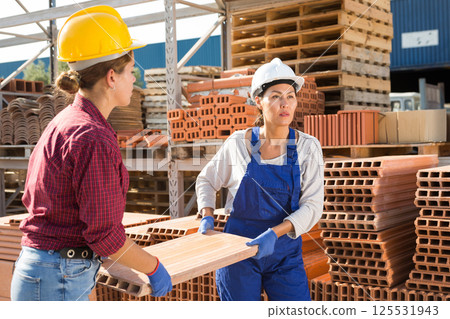 Construction warehouse female workers carry brick pallets on territory of open-air site 125531943