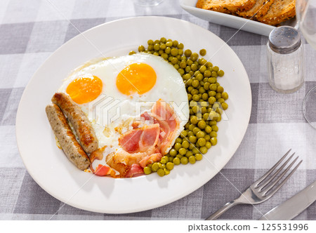 Hearty homemade breakfast - fried eggs with bacon, toasted sausages and large portion of green peas 125531996
