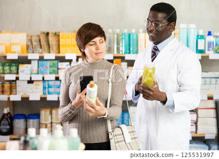 Woman buyer scans shampoo or shower gel qr code with pharmacist Woman buyer scans shampoo or shower gel qr code with pharmacist 125531997