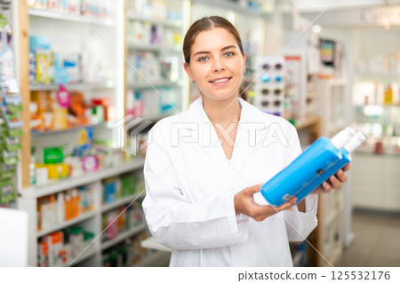 Portrait of a smiling young female pharmacist, demonstrating recently received goods for sale Portrait of a smiling young female pharmacist, demonstrating recently received goods for sale 125532176
