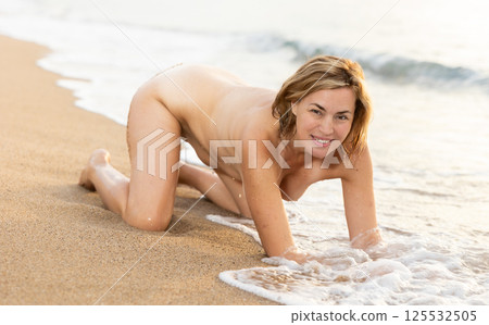 Completely naked girl sitting on sand against sea 125532505