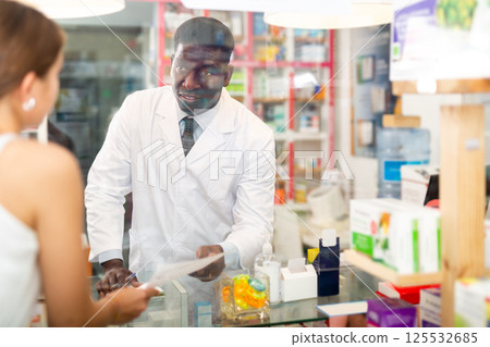 African american male pharmacist takes a prescription for medicines from a customer African american male pharmacist takes a prescription for medicines from a customer 125532685