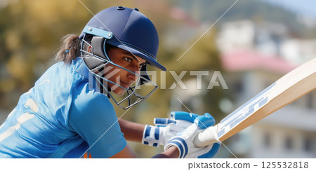 Female cricketer, blue uniform, batting, helmet, sports field, intense focus, outdoor action 125532818