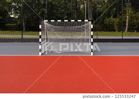 A red court featuring a freshly constructed soccer goal in a park setting 125533247