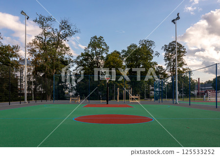 Empty basketball court with a vibrant green surface at sunset in a public park 125533252