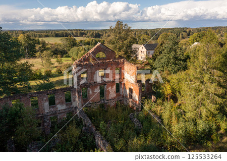 Abandoned brick building surrounded by lush greenery in rural landscape at golden hour 125533264