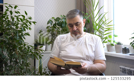 Man Reading Book in Armchair Surrounded by Indoor Plants 125533295