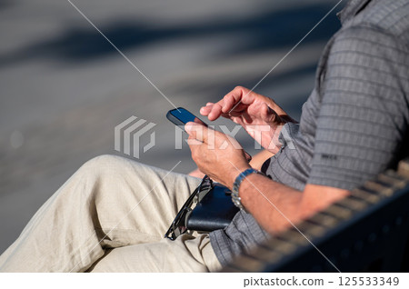 Individual engaged with a smartphone outdoors, enjoying a sunny day with another person. Individual engaged with a smartphone outdoors, enjoying a sunny day with another person. 125533349