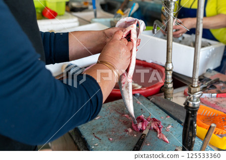 Fish being cleaned at a bustling market with vendors and fresh seafood during daytime Fish being cleaned at a bustling market with vendors and fresh seafood during daytime 125533360