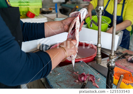 A person skillfully filleting fish at a bustling market stall during the morning hours. 125533543