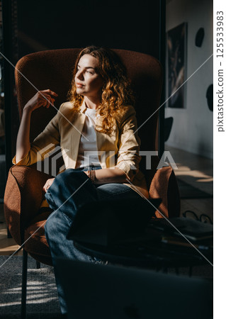 A young woman with curly red hair sits in a high-backed chair looking contemplatively to the side. Vision and clarity, decision-making moments, innovation leadership, women in strategy... 125533983