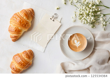 Fresh croissants, coffee and a note in a chic flat lay, capturing the essence of a Parisian morning 125534364