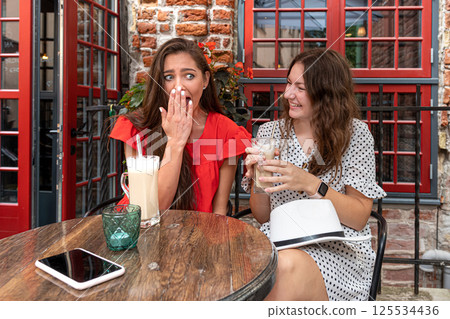two young girls share a secret in the ear sitting in a cafe, girls party concept two young girls share a secret in the ear sitting in a cafe, girls party concept 125534436