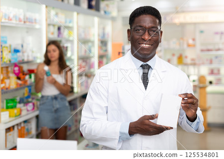 Portrait of african american male pharmacist in pharmacy demonstrating goods 125534801