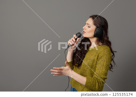 cheerful young woman in casual clothes with headphones sing song in microphone, mock up copy space cheerful young woman in casual clothes with headphones sing song in microphone, mock up copy space 125535174