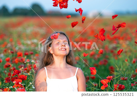 cute girl wearing white dress in summer blooming poppy field playing under evening sun 125535321