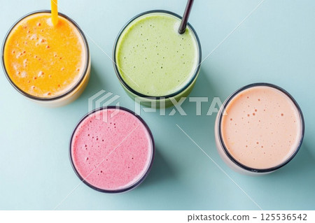 Refreshing flat lay of vibrant smoothies with colorful fruits on a pastel blue surface 125536542