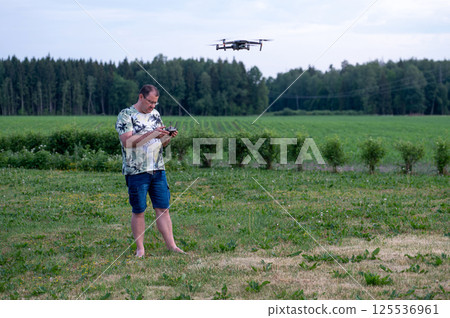 A man operating the drone by remote control on the meadow near forest. A man operating the drone by remote control on the meadow near forest. 125536961