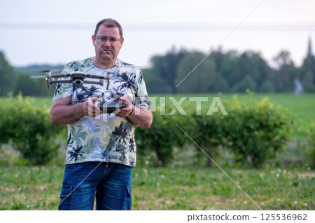 A man operating the drone by remote control on the meadow near forest. A man operating the drone by remote control on the meadow near forest. 125536962