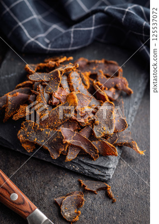 Beef jerky. Dried spiced meat on black table. 125537072