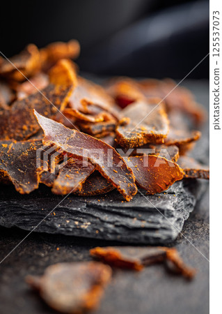 Beef jerky. Dried spiced meat on black table. Beef jerky. Dried spiced meat on black table. 125537073