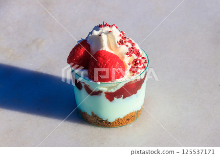 Strawberry trifle with whipped cream, berry sauce and cookie crumbs in a glass on a gray concrete background 125537171