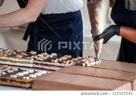 Baker decorating chocolate cake with piping bag. Shallow depth of feld Baker decorating chocolate cake with piping bag. Shallow depth of feld 125537241