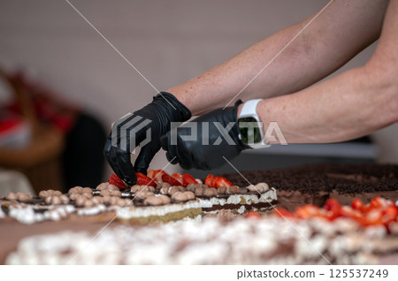 Person decorating cake with strawberries. Background with selective focus and copy space. 125537249