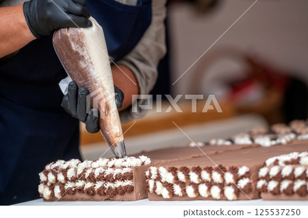 Baker decorating chocolate cake. Background with selective focus and copy space. Baker decorating chocolate cake. Background with selective focus and copy space. 125537250