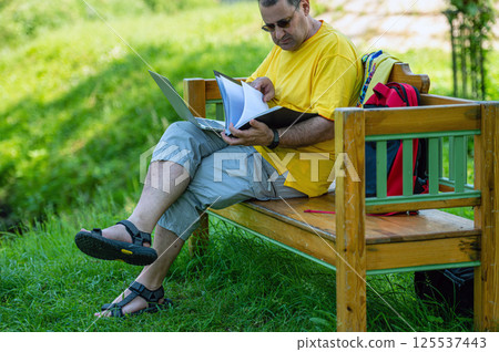middle aged man with laptop and documents working outside in garden, green home office concept. middle aged man with laptop and documents working outside in garden, green home office concept. 125537443
