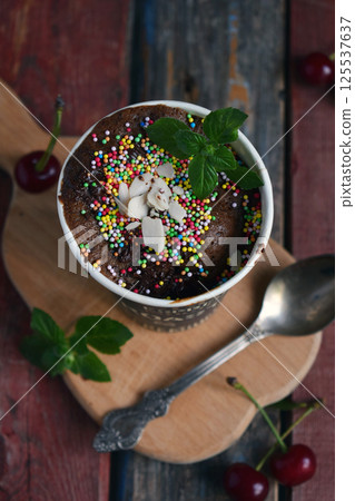 Chocolate dessert topped with whipped cream colorful sprinkles and mint served in a coffee cup on rustic wooden boards perfect for sweet cafe menus bakery advertisements and cozy food presentations 125537637