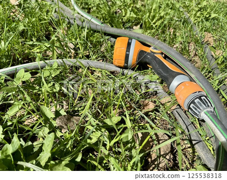 Garden Hose and Spray Nozzle on Grass for Watering 125538318