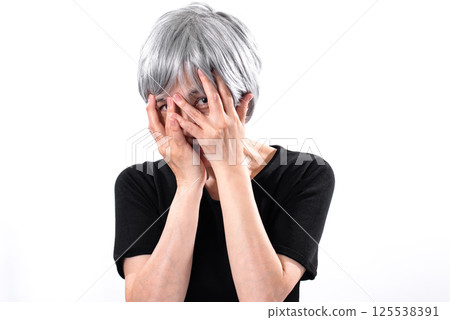 Senior woman glancing at someone while covering her face with her hands Senior woman glancing at someone while covering her face with her hands 125538391